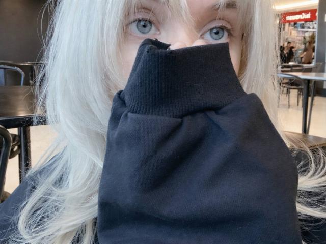 Hortencia Vergin, avec ses cheveux blonds, ses yeux bleus et son pull noir, cachant son nez et sa bouche avec le pull, est assise dans un café. Ses seins sont partiellement visibles..
