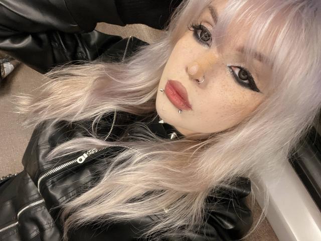 HortenciaVergin a les cheveux d'un rose pâle, du khôl noir, un anneau au nez, des piercings aux lèvres et des taches de rousseur. Elle porte une veste en cuir noir avec une fermeture éclair et regarde l'appareil photo..