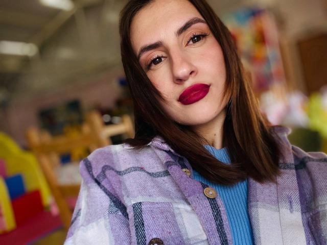 PreciousLambrecht heeft rechtbruin haar, bruine ogen en rode lippenstift. Ze draagt een paars geruit jasje over een blauw gestreept shirt. Haar borsten zijn niet zichtbaar..