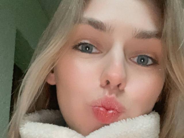 Sandas Haysletts schmollender Gesichtsausdruck mit vollen, rosafarbenen Lippen, blauen Augen und blonden Haaren, sie trägt eine flauschige weiße Kragen und macht ein Küssengesicht in einem Selfie..