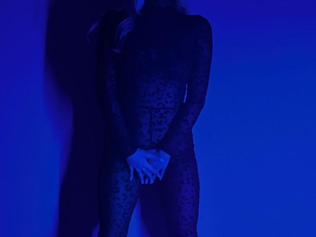 BalletSwan está de pie, vestida con un body de leopardo transparente en color azul oscuro, con las manos juntas, cubriendo sus genitales, con senos apenas visibles, en penumbra y misteriosos, con el cabello rubio largo, iluminación azul, sensual, provocativo..