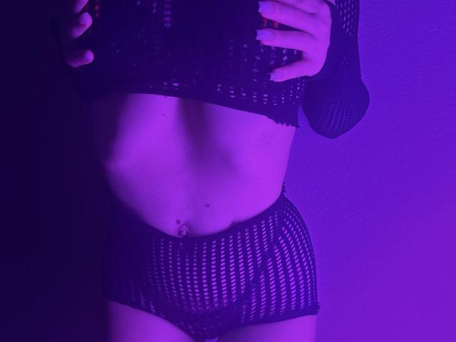 BalletSwan in purple-lit shot wearing black mesh top and shorts, hands on chest, showing flat midriff with belly button piercing, focused on her torso and lower body.