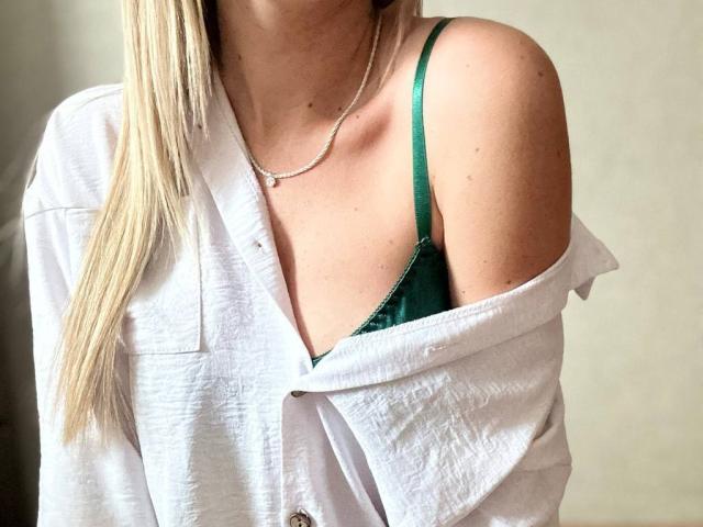 BalletSwan with blonde hair, white shirt off-shoulder, green bra strap, slim neck, delicate necklace, showing her tits. Soft light, casual vibe.