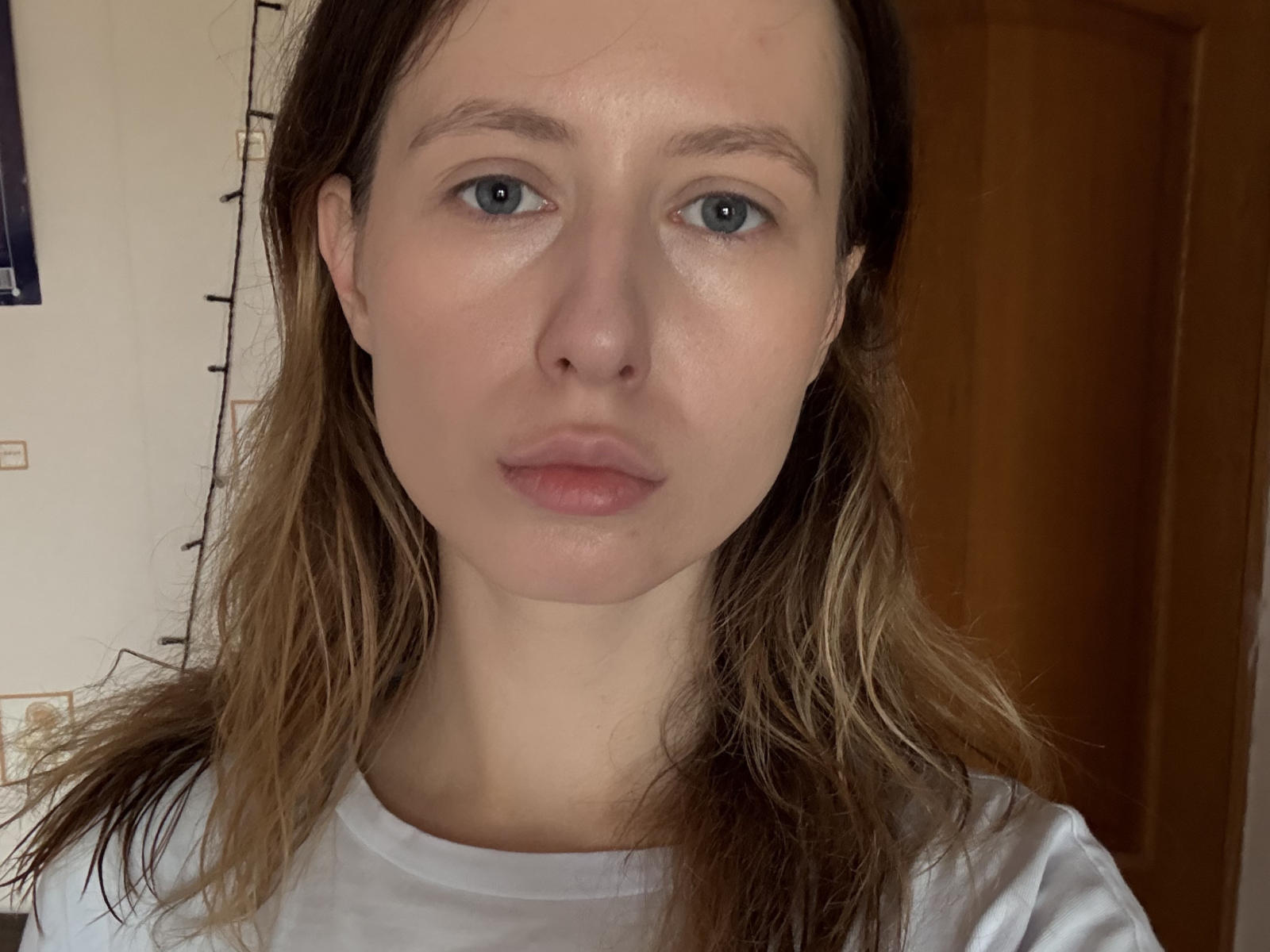 Reanna Dreben tem pele clara, olhos azuis e lábios levemente inchados. Ela está vestindo uma camisa branca, com cabelo loiro claro e ondulado. O rosto dela está centralizado na foto..