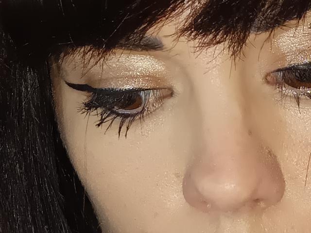 Gli occhi di OrianaLaFrancaise, con ciglia marrone scuro, eyeliner nero lucido e ombretto dorato brillante, sono rivolti verso il basso, mostrando un viso umido e leggermente lucido con capelli neri..