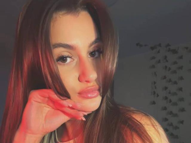Ellen Kienbaum ha le unghie dipinte di rosso, labbra rosa lucide e lunghi capelli castani, con una mano appoggiata sulla guancia, che guarda nella fotocamera con occhi marroni seducenti..