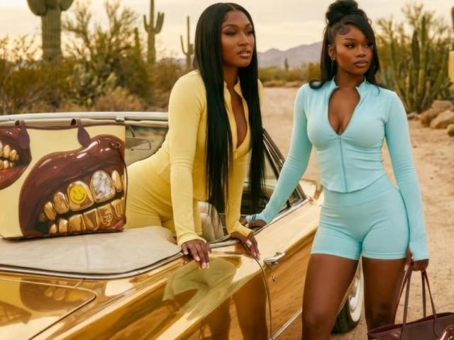 Two CoochieFlames with long black hair, wearing tight yellow and blue outfits, leaning on a gold car. One has large yellow boots, the other holds a purple bag.