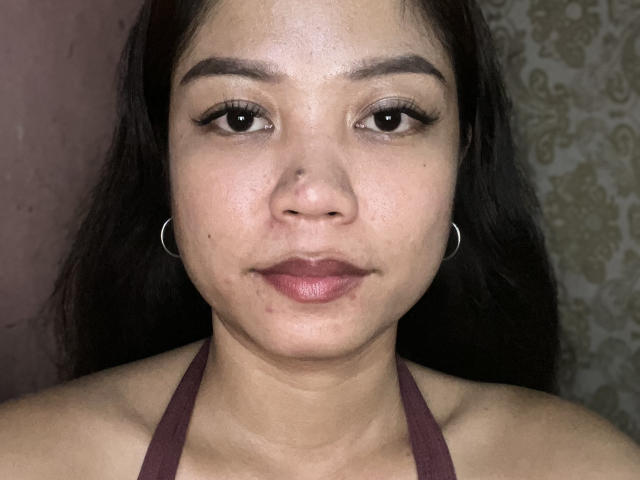 Venessa Gondran, con piel de tono marrón medio, ojos oscuros y cabello negro largo, vestida con un top de tirantes color burdeos, pequeños aros y un rostro ligeramente sonrojado, mirando directamente a la cámara..