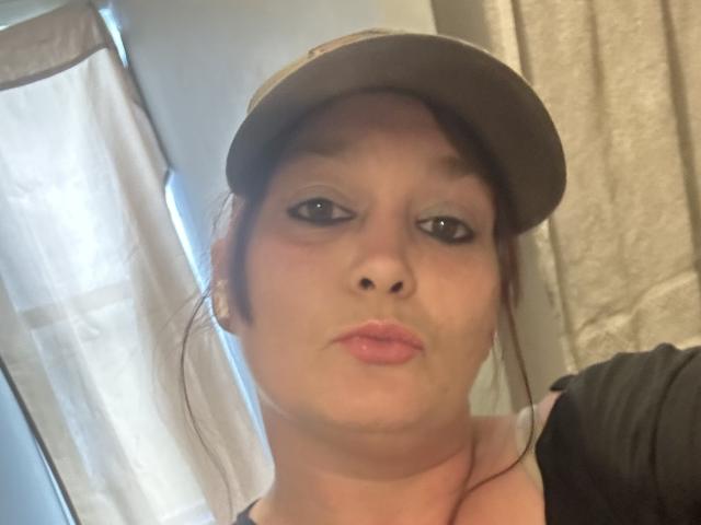 Ashlleyy69, con los labios fruncidos, lleva un gorro plano, el cabello castaño recogido en un moño despeinado, una blusa negra y un maquillaje ligero. Tiene ojos azules y labios rosados, en un selfie..