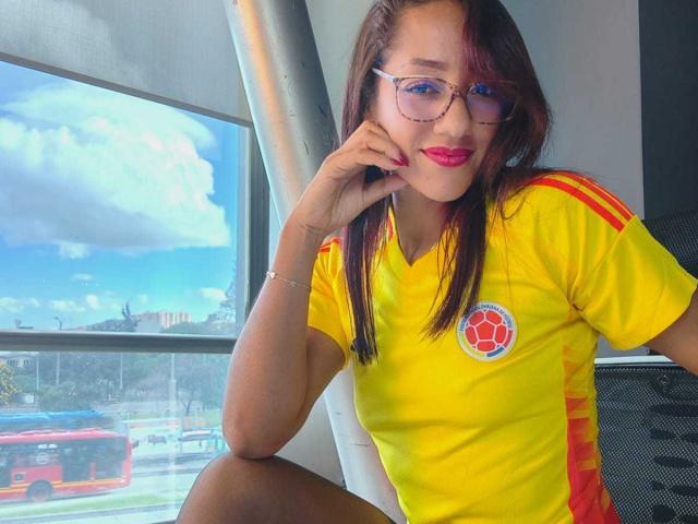 SamanthaCorine met rode lippenstift, een bril en een geel voetbalsok, zittend bij het raam, hand op haar wang, waarbij haar borsten zichtbaar zijn, reflectie van een bus buiten, zonnige dag, ontspannen..