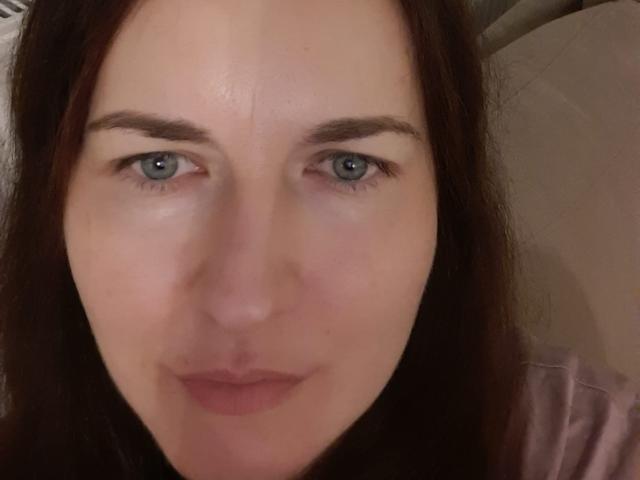 NadiaRoses Gesicht mit blauen Augen, brauen Augenbrauen und leicht rosafarbener Haut. Sie hat langes, braunes Haar und ein leichtes Lächeln. Ihre Nase ist klein und ihre Lippen sind rosa..