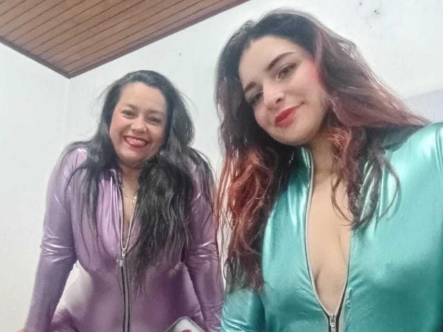 SaraAndMarilyn69 ont de longs cheveux noirs, et portent des combinaisons brillantes violettes et vertes avec des fermetures éclair, avec des décolletés en V profonds, et sourient à l'appareil photo. Les seins sont visibles à travers les fermetures éclair des combinaisons..