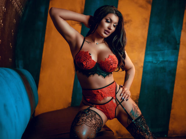 ItsJessieBabe in rode kant lingerie, die haar borsten en billen laat zien, met kant hoge knie sokken, hand op haar hoofd, een sexy pose, donker golvend haar en een verleidelijke uitdrukking, in een donkere kamer..