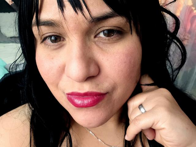 Viviana Thompson tem cabelo preto, olhos castanhos, lábios rosados e brilhantes, e um anel de prata na mão direita. Sua pele tem algumas sardas. Ela está olhando para a câmera com um leve sorriso..