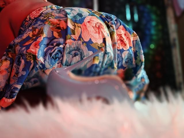 AmberSunshine's floral butt, covered in blue, pink, and white rose-patterned fabric, is prominently in the foreground, with a blurred white surface below.