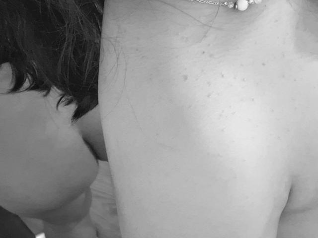 NekoPam's bare shoulders with small freckles, wearing a necklace, and dark hair in the background, showing a partial view of her tits and upper body. Black-and-white photo.