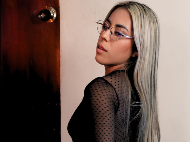 Incontro veloce con una ragazza dai lunghi capelli biondi, occhiali e una maglietta nera a pois, che si guarda indietro, mostrando il sedere. Il suo viso è leggermente girato, con un'espressione seducente..