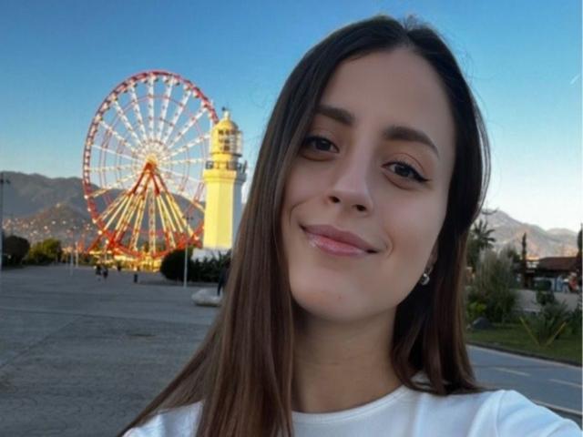 CarynHowkins a de longs cheveux bruns, un joli sourire, et porte une chemise blanche. Elle se tient devant une grande roue colorée et un phare jaune..