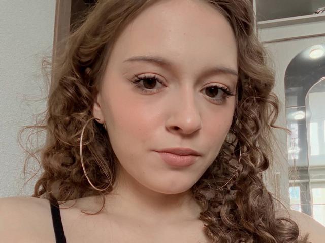 ShawandaClester heeft krullend bruin haar, roze oorringen en een rustige uitdrukking met roze lippenstift. Haar bruine ogen en lichte blos zijn opvallend. Ze draagt een zwarte top..