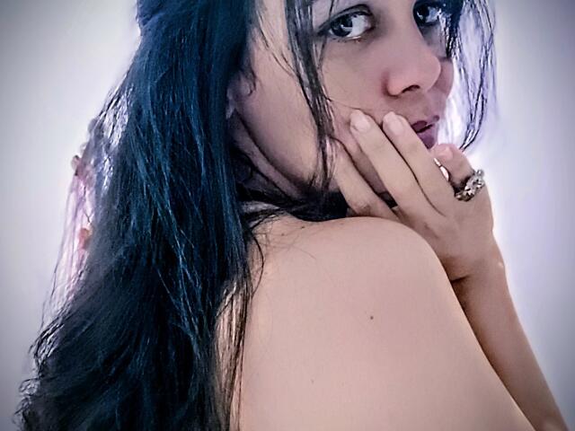 AuraCatherine with wet black hair, covering her face with her hand, showing off a ring, looking over her shoulder, her bare shoulder visible, subtle light on her skin.