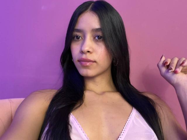 LaurentRay has long black hair, pink lace top, small tits, light brown skin, and red nails, sitting against a pink and purple gradient background with a relaxed expression.