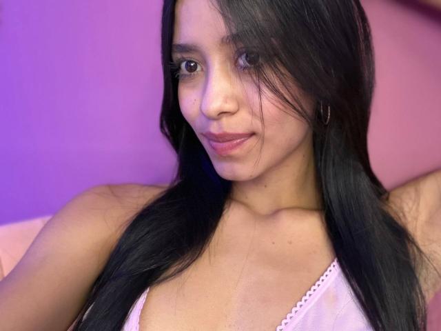 LaurentRay has long black hair, brown eyes, and a slight smile. She's wearing a pink, lace-trimmed top, showing her tits and a small hoop earring.