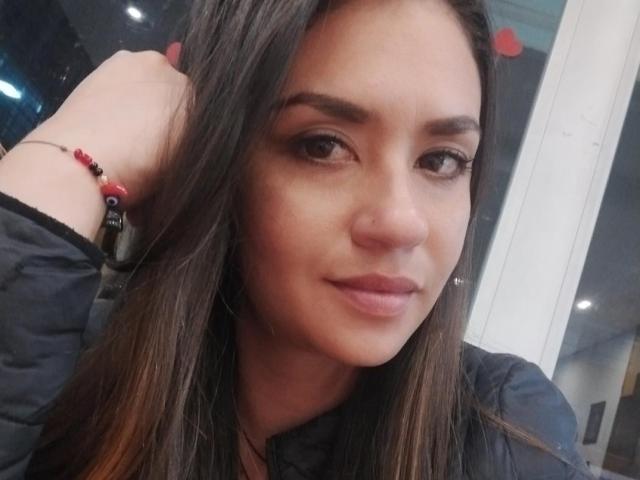 TheresaLarson heeft bruin haar, een schattige neus en volle lippen met een lichte glimlach. Ze draagt een zwarte, gewatteerde jas en een rode kralenarmband om haar rechterhand..