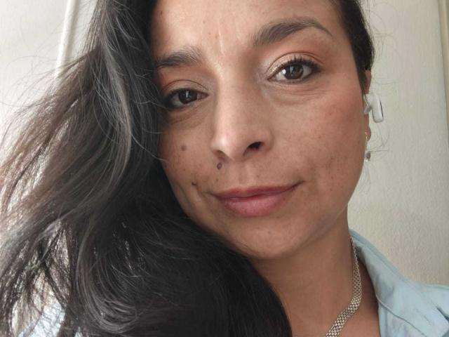 StangelarRivera a les cheveux noirs et ondulés, les yeux marron et un sourire discret. Elle a de petites taches de rousseur sur le nez et la joue, et porte une chemise bleu clair et un collier en argent..