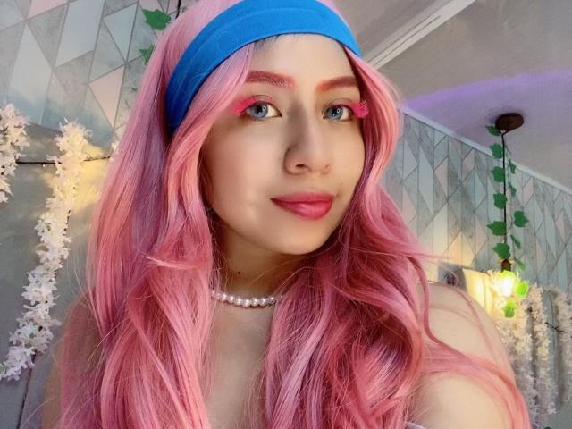 ZoeRedds with pink hair, blue headband, pink eyeliner, pearl necklace, smiling, showing tits, in a cute selfie, wearing pink lipstick, looking cute and sexy.