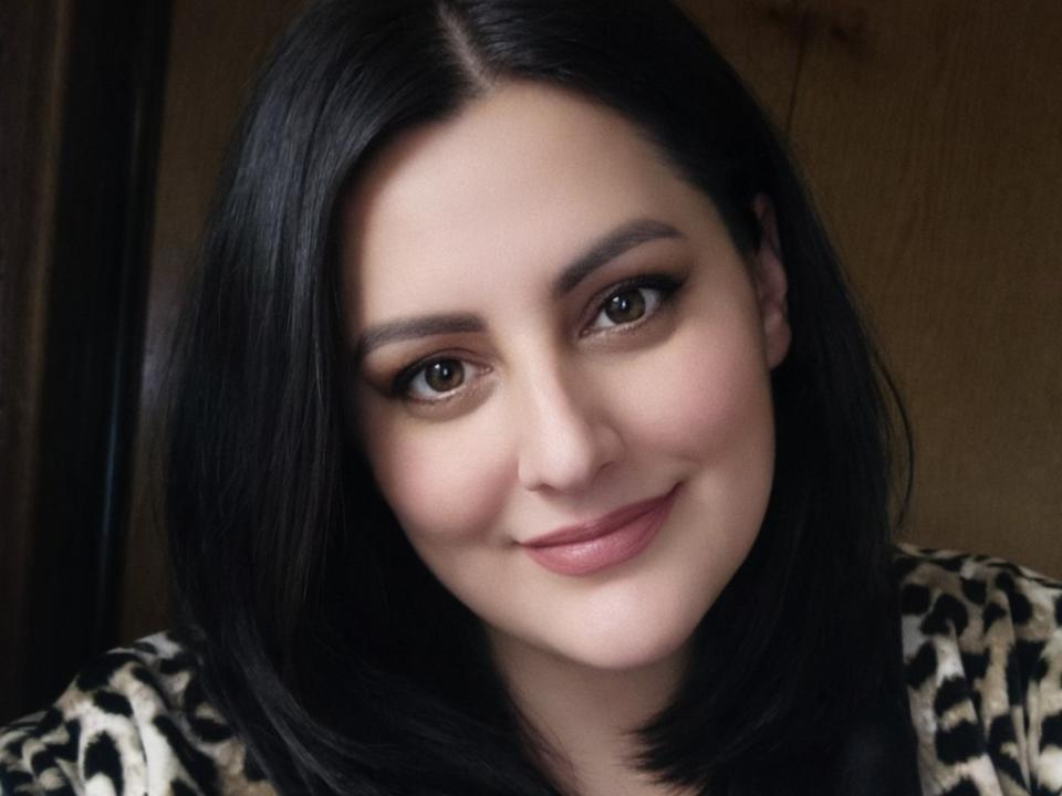 ChristianNetta tem cabelos pretos de comprimento médio, olhos castanhos e um sorriso adorável. Ela está vestindo uma blusa com estampa de leopardo e tem uma pele clara. Seus seios são pequenos e ela é atraente..