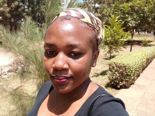 ClaireJulie hat glänzende, braune Haut, dunkle Augen, rosafarbenen Lippenstift und trägt einen Kopftuch mit Zebramuster, ein schwarzes Oberteil und eine rote Halskette. Sie ist draußen und umgeben von Grün..