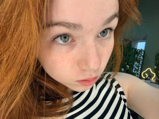 Il viso di KatiRokisky, con la pelle chiara e lentiggini rosse, occhi azzurri e capelli rossi, indossa una maglietta a righe bianche e nere, con un leggero sbuffo e un'espressione carina e seria..