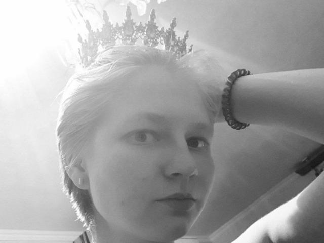 Laila Lafreniere, com cabelo loiro curto, usando uma coroa ornamentada e uma pulseira no braço direito, com uma expressão séria em uma foto em preto e branco..