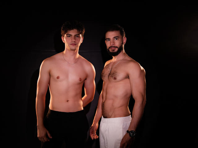 Dois homens sem camisa, BASTIANs, em pé contra um fundo escuro. O BASTIAN à esquerda usa calças pretas, não tem pelos no peito e tem uma constituição física leve. O BASTIAN à direita usa calças brancas, tem barba e pelos no peito..