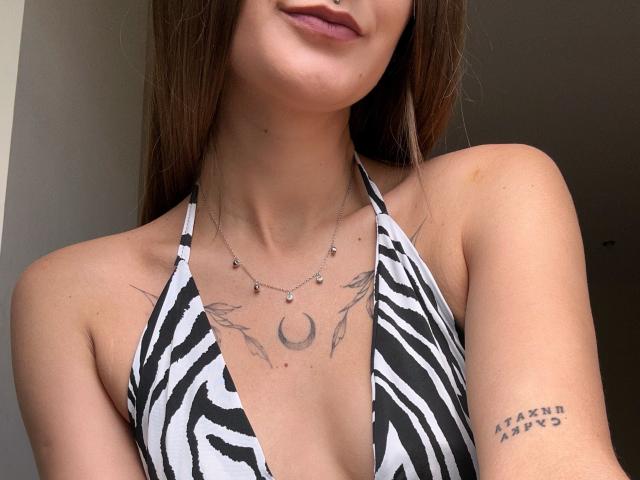 Karish, avec ses cheveux bruns, porte un haut de bikini à rayures zébrées, et on peut voir des tatouages sur sa poitrine et son bras, ainsi qu'un collier avec de petites perles. Ses seins sont partiellement visibles..