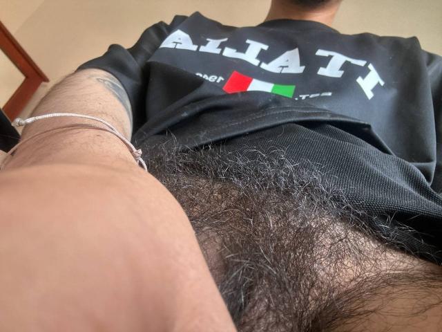 Les boules poilues de ZacWatson, en chemise noire, prises sous un angle bas, montrant un bras tatoué et un bracelet en argent. Le pénis de ZacWatson n'est pas visible..