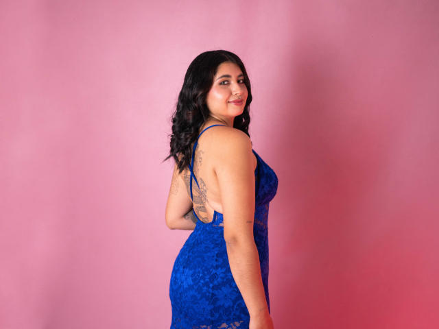 Valery Silva indossa un abito blu in pizzo, che mette in mostra il suo sedere, un tatuaggio sulla schiena e sorride alla fotocamera. Ha capelli scuri e ondulati e un viso carino..