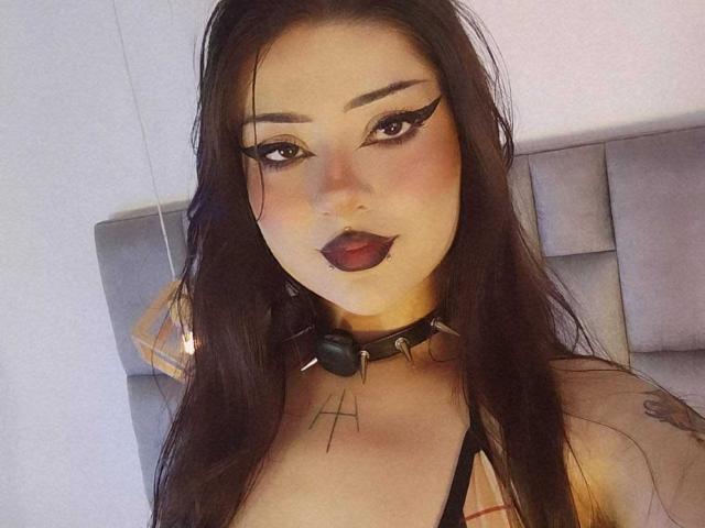 Helena Morningstar trägt dunkelroten Lippenstift, starken Eyeliner und langes, schwarzes Haar. Sie trägt eine schwarze Halskette mit einem Ball und Stacheln und zeigt ein Tattoo unter ihrer Brust..