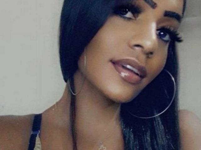 SarahMorena hat dunkle Haut, langes schwarzes Haar, dicke Augenbrauen, große Wimpern, glänzliche braune Lippen, Ohrringe im Stecker-Stil und ein süßes Lächeln. Sie trägt ein schwarzes Top mit Trägern..