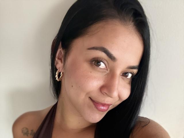 HikariChloe heeft donker haar, bruine ogen en een schattige glimlach met roze lippenstift. Ze draagt gouden oorringen en een bruin topje met halter, waar een kleine tatoeage zichtbaar is..