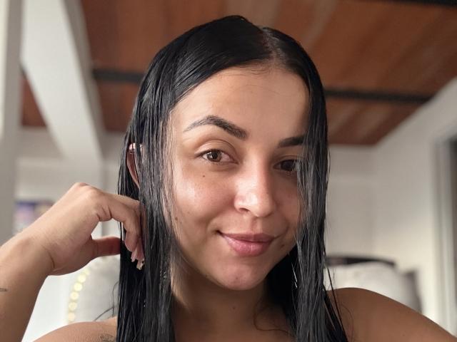 HikariChloe tiene el cabello negro y lacio, piel de color marrón claro y una nariz pequeña. Está sonriendo, con la mano cerca de la oreja, mostrando un tatuaje discreto en el hombro..