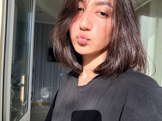 HeikeCarchi with puffy lips, medium brown bob, black shirt, sunlit face, light freckles, slight blush, relaxed expression, soft natural light, slight shadow on left side of face.