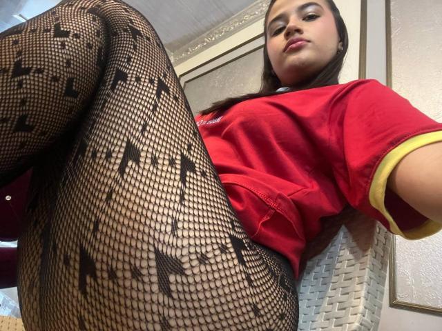 IrisBlair in a red shirt with yellow sleeves, wearing black fishnet tights with star patterns, taking a low-angle selfie, showing her taut ass and confident expression.