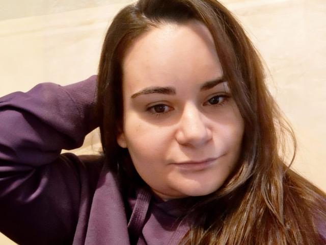 ElizanXStarzy met bruin haar, een paarse hoodie, en een subtiele grijns, met haar in haar handen, zachte huid, lichtbruine ogen en een subtiele glimlach. Haar neus is iets omhoog gekeerd..