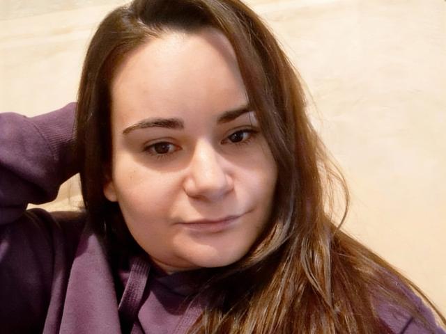 ElizanXStarzy tem cabelo castanho, um nariz delicado e um sorriso discreto, vestindo um suéter roxo, com uma mão atrás da cabeça. Ela parece relaxada e atraente..