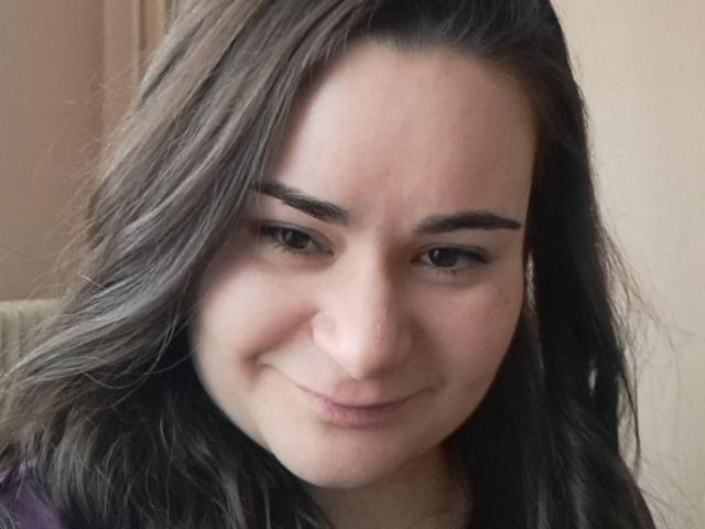 El rostro de ElizanXStarzy, mostrando una sonrisa sutil con cabello oscuro y ondulado, cejas gruesas y un tono de piel claro, vestida con una blusa morada, en un selfie casual..