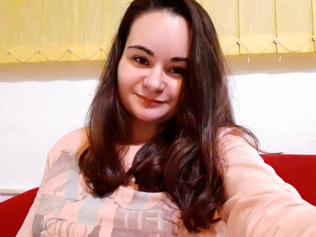 ElizanXStarzy, con cabello largo y castaño, sonriendo, vestida con una camisa rosa de manga larga, tomando una selfie, mostrando su pecho en la foto..