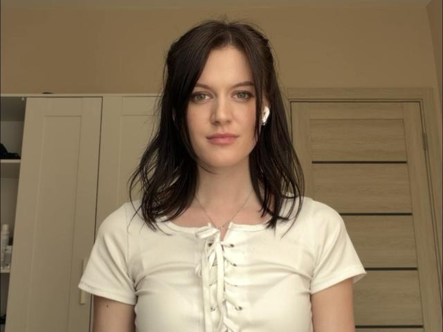 LachelleCaraker tem pele clara, cabelo castanho escuro até os ombros, olhos verdes e pequenos brincos brancos. Ela veste uma camisa branca com cadarços, que mostra seus pequenos seios. Ela está em pé em um quarto..