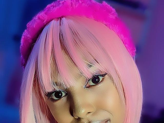 MissAniaSexy ha i capelli rosa, un berretto rosa soffice e gli occhi scuri. Il suo viso è leggermente inclinato con un sorriso appena accennato. La sua pelle è liscia e luminosa..