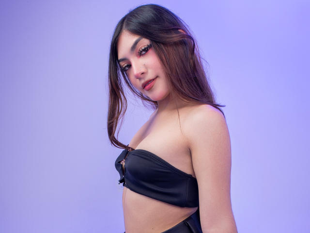 LunaRosseX com cabelo castanho escuro, usando um sutiã preto sem alças, mostrando seios pequenos, pele clara, sorriso discreto, fundo roxo, cabeça levemente virada, olhando para a câmera..